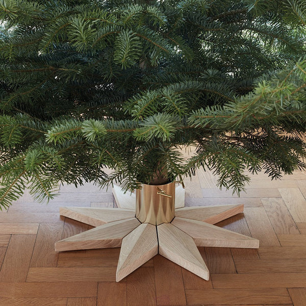 Wooden star-shaped Christmas tree stand with natural wood tones and a modern design. Green foliage enhances the festive look.