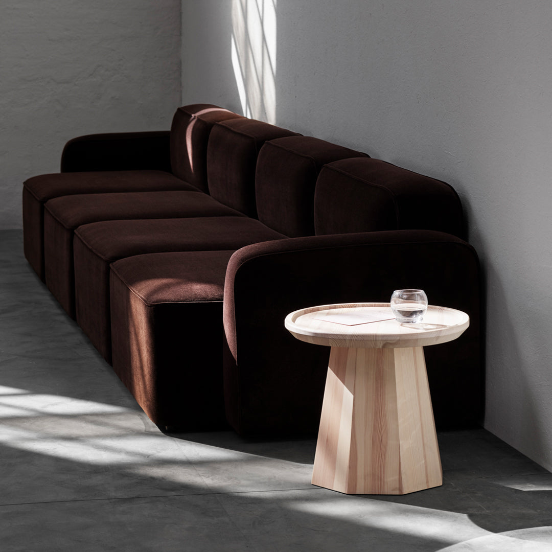 Dark brown velvet sofa with soft, rounded shapes, paired with a light wooden side table in a minimalist setting.