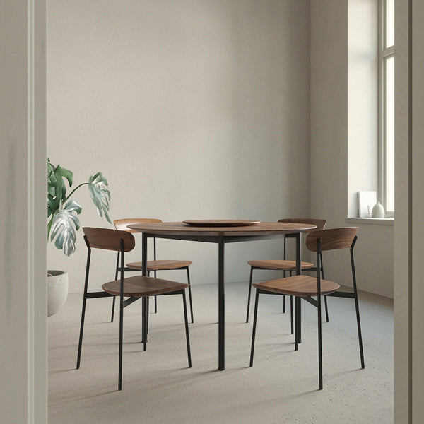 Modern round wooden table with black metal legs, complemented by four minimalist brown chairs, in a neutral-toned room.