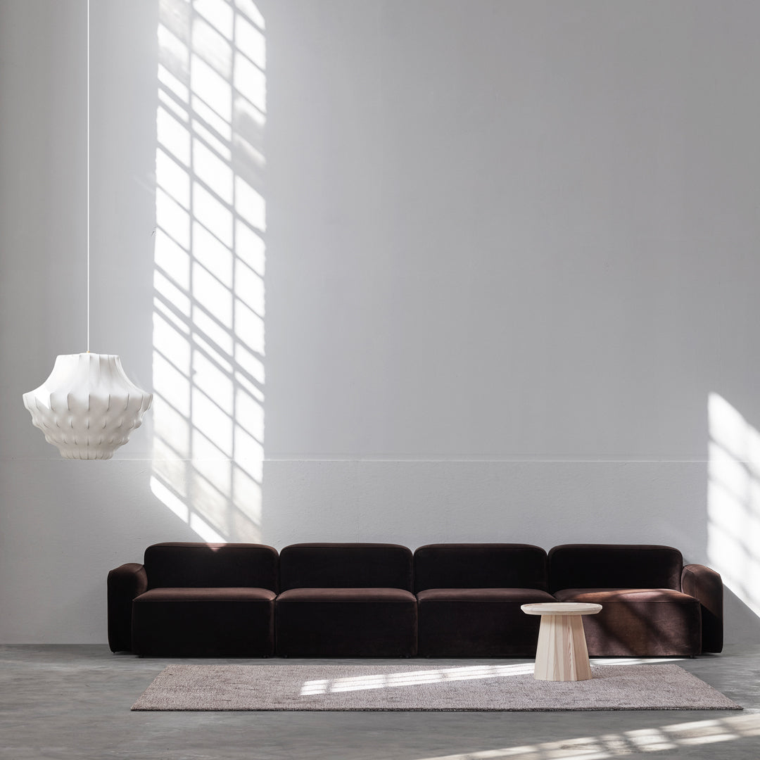 Luxurious dark brown velvet sofa with smooth lines, paired with a light-colored round table and soft gray rug.