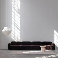 Luxurious dark brown velvet sofa with smooth lines, paired with a light-colored round table and soft gray rug.