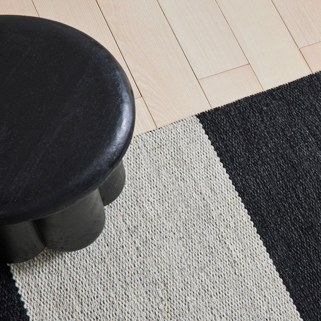 Black and cream striped rug with textured patterns, set on a light wooden floor.