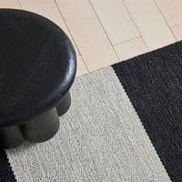 Black and cream striped rug with textured patterns, set on a light wooden floor.