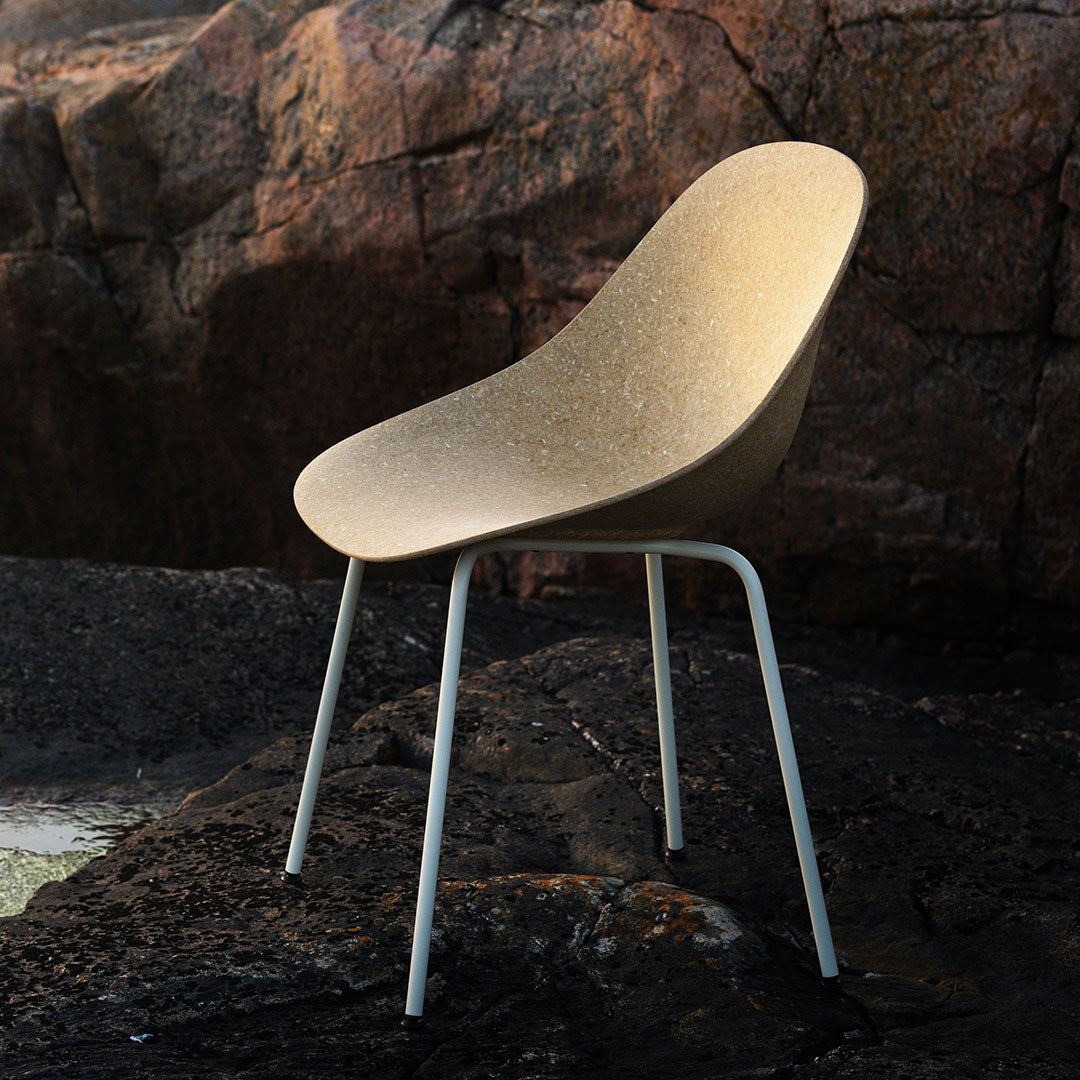 Beige ergonomic chair with a smooth finish and sleek white metal legs, set against a rocky background.