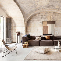 Modern living room featuring brown sofa, neutral patterned rug, and earthy tones in artwork. Natural light enhances warmth.