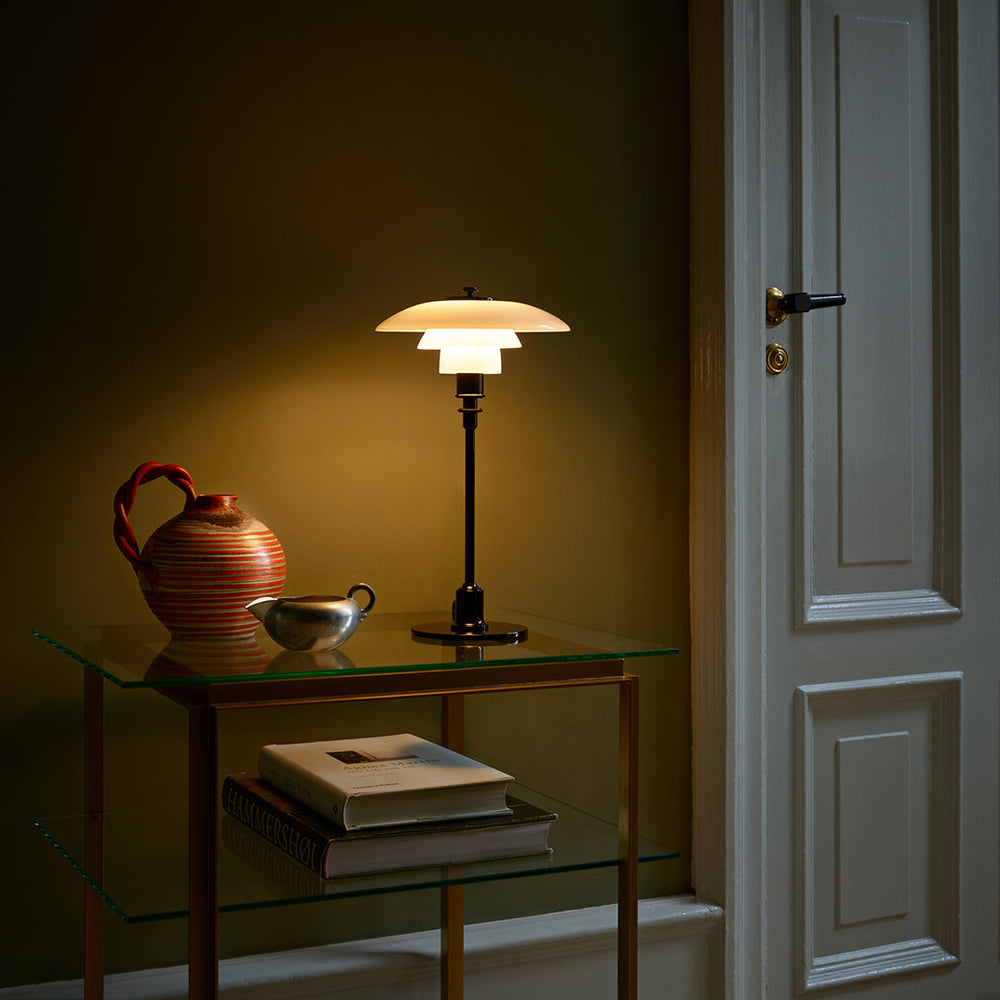 Stylish table lamp with a cream shade, black base, and warm light, alongside decorative terracotta and silver vessels.