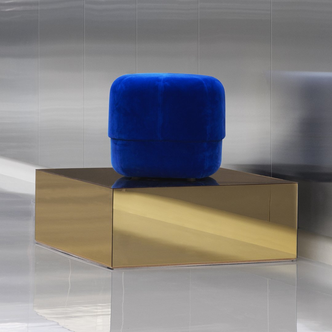 Vibrant blue velvet pouf on a sleek gold cube, highlighting modern colors and minimalist design elements.