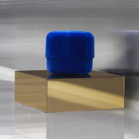 Vibrant blue velvet pouf on a sleek gold cube, highlighting modern colors and minimalist design elements.