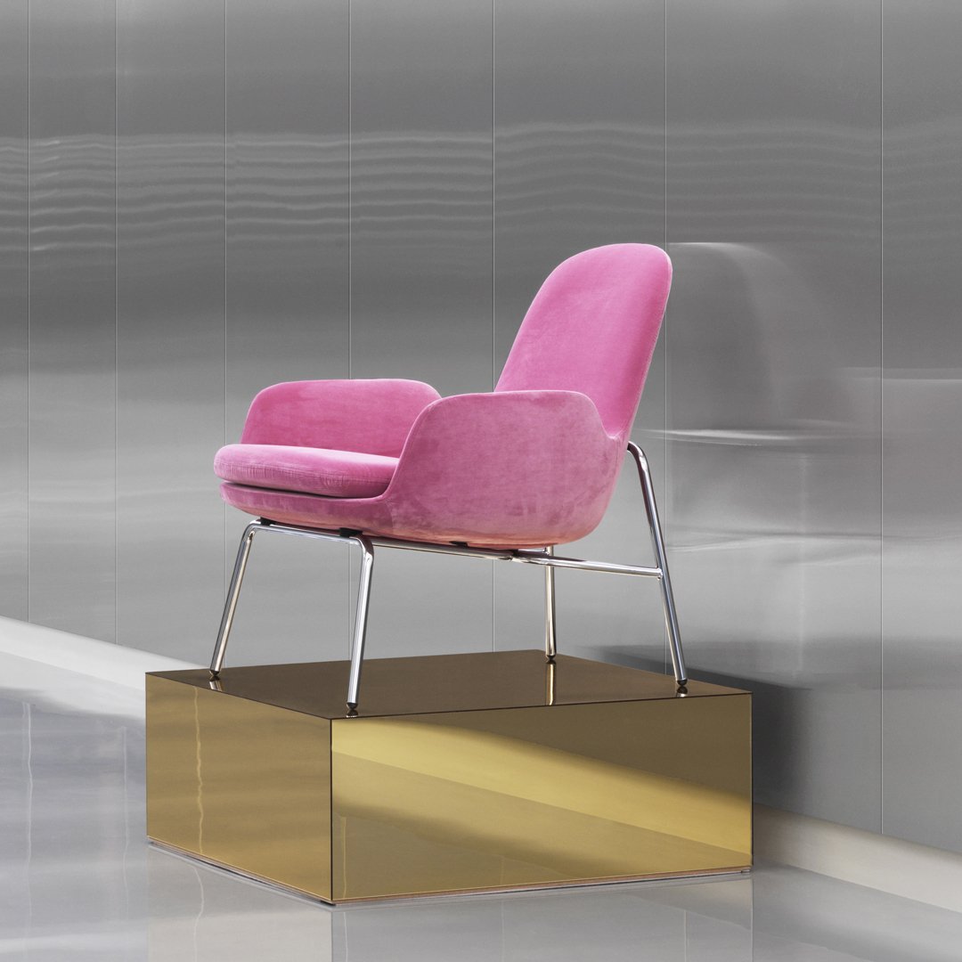 "Stylish pink velvet chair with sleek metallic legs on a modern gold display pedestal."