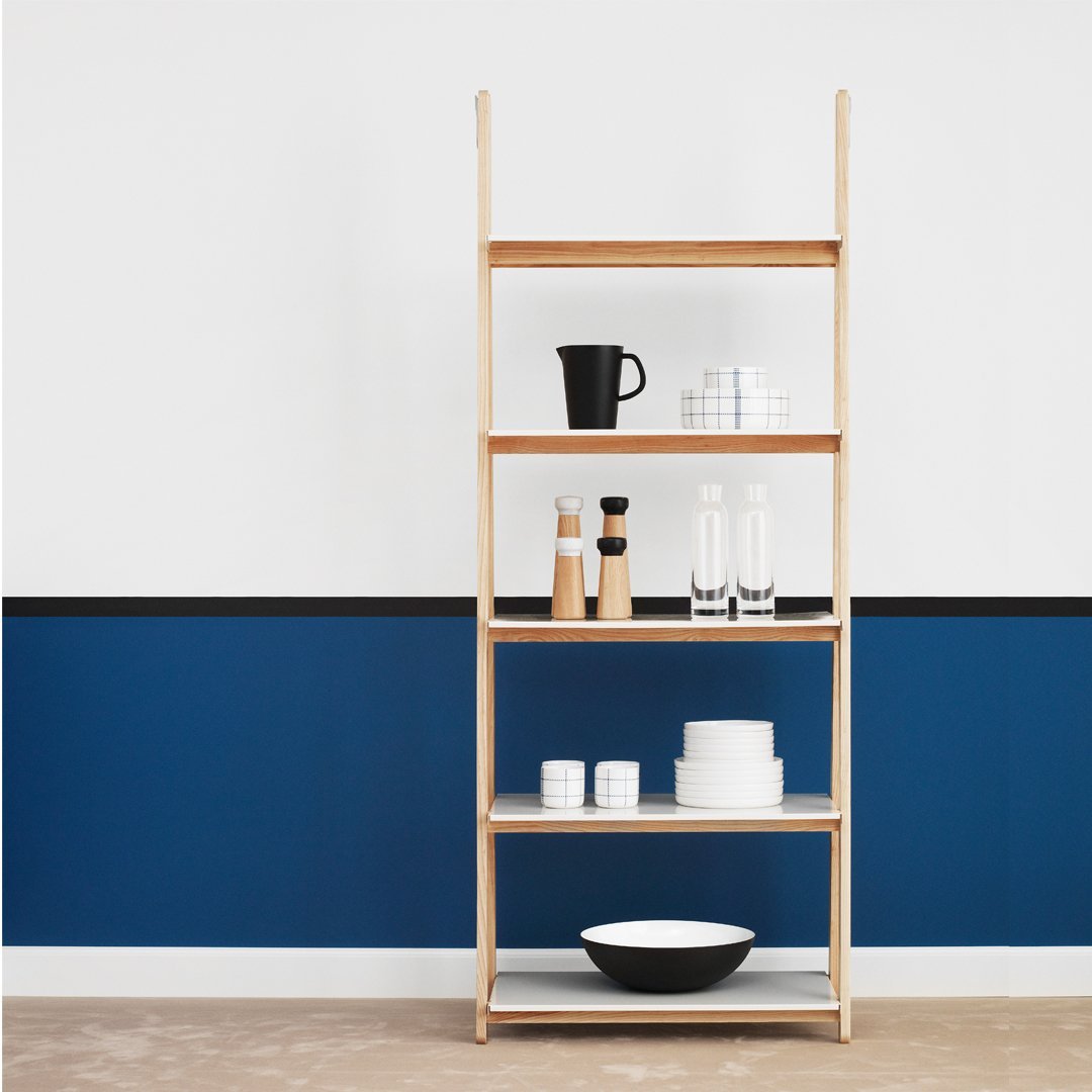 Natural wood shelving unit with white dishes and glassware against a deep blue wall, featuring a stylish, minimalist design.