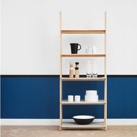 Natural wood shelving unit with white dishes and glassware against a deep blue wall, featuring a stylish, minimalist design.