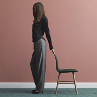 Stylish black top and grey patterned trousers against a soft pink wall and teal carpet. Elegant chair in green.
