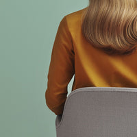 Mustard yellow shirt against a soft green background, with a sleek gray chair in view. Elegant and modern color palette.