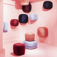 Colorful poufs in shades of pink, burgundy, blue, and lavender with geometric patterns against a soft pink backdrop.