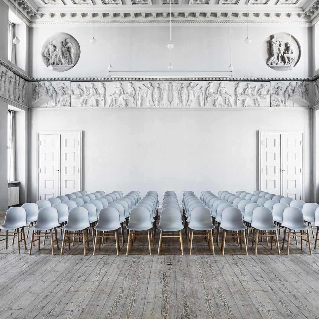 Light gray chairs in a minimalist setting with wooden legs, arranged in neat rows on a wooden floor.