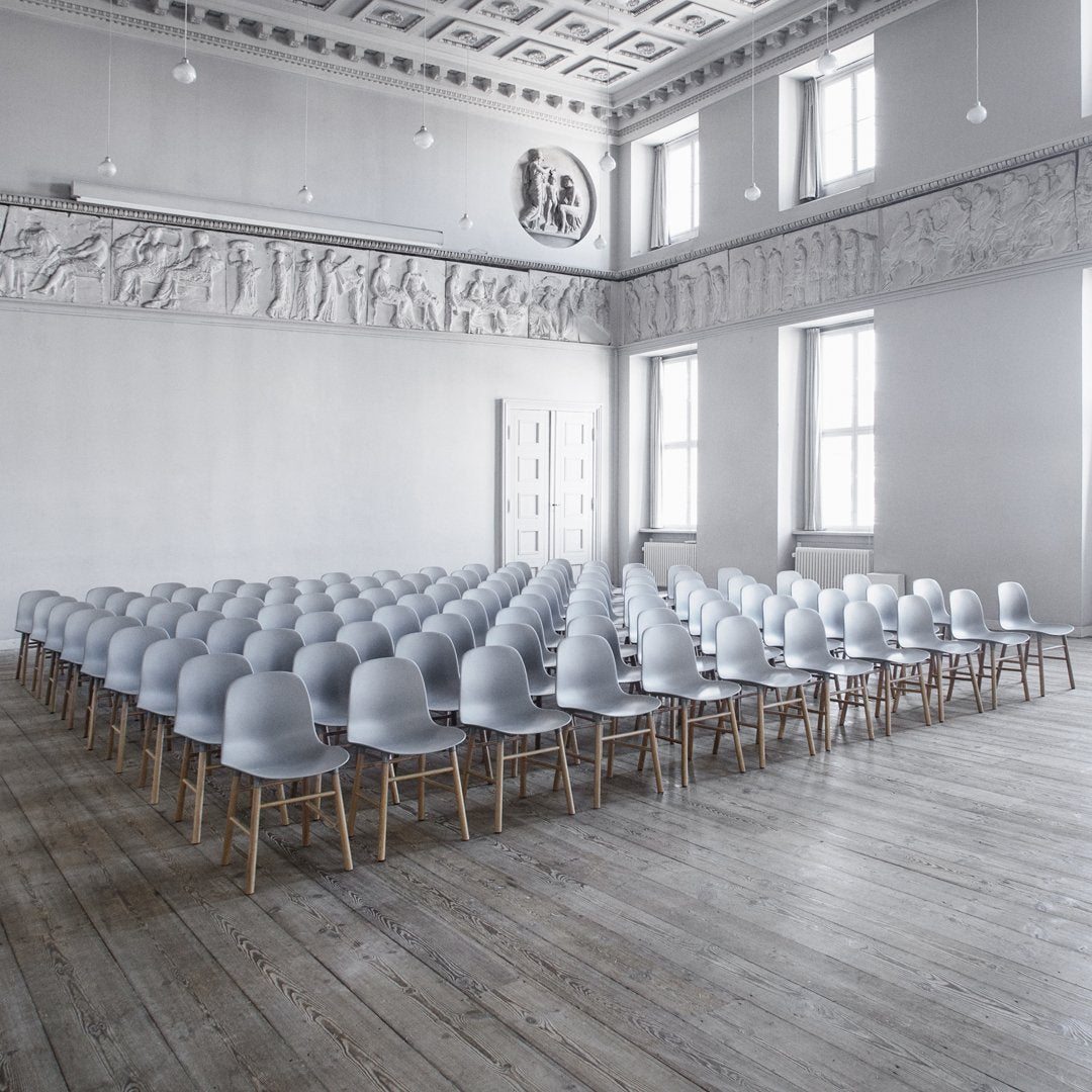 Gray chairs with wooden legs arranged in a minimalist, light-filled space featuring white walls and wooden floors.