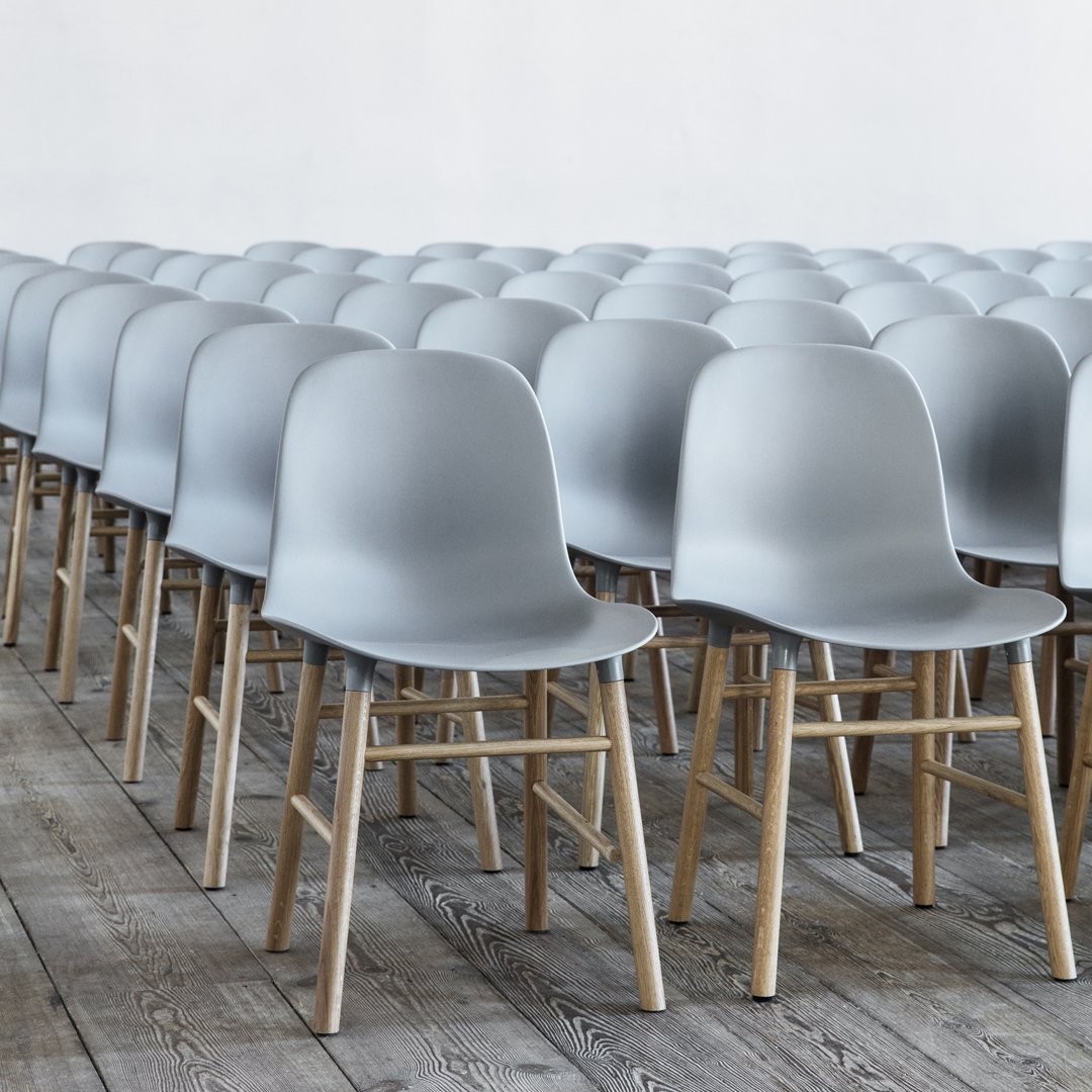 Minimalist gray plastic chairs with light wooden legs arranged in a neat row on a wooden floor.