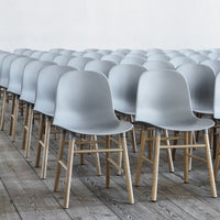 Minimalist gray plastic chairs with light wooden legs arranged in a neat row on a wooden floor.