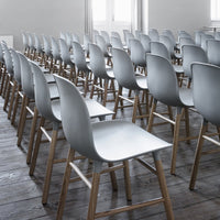 Gray plastic chairs with wooden legs arranged in a neat, orderly row on a wooden floor.