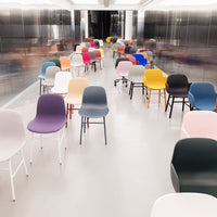 Colorful chairs in various shades of pink, blue, purple, yellow, green, and grey arranged in a modern hallway setting.