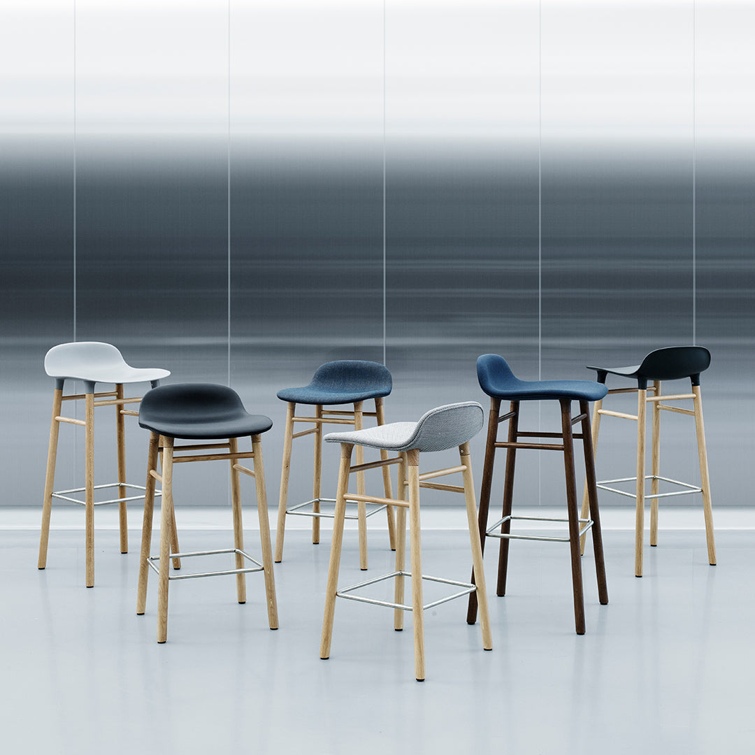 Modern bar stools in white, gray, navy, and black with natural wood legs, set against a gradient gray background.