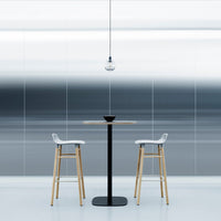 Modern bar table and stools with sleek wood and black accents against a gradient blue and gray patterned background.