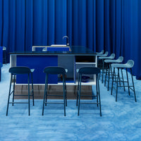Modern kitchen island with deep blue accents, black countertops, and sleek gray bar stools against a vibrant blue backdrop.