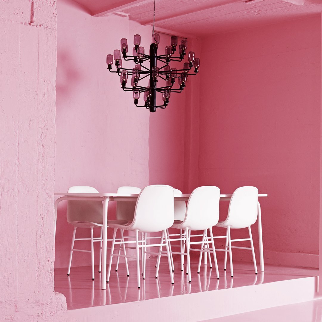 White dining chairs contrast against a vibrant pink backdrop with a stylish black chandelier above.