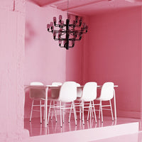 White dining chairs contrast against a vibrant pink backdrop with a stylish black chandelier above.