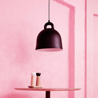 Black pendant lamp against a soft pink wall, with a minimalist wooden table featuring salt and pepper shakers.