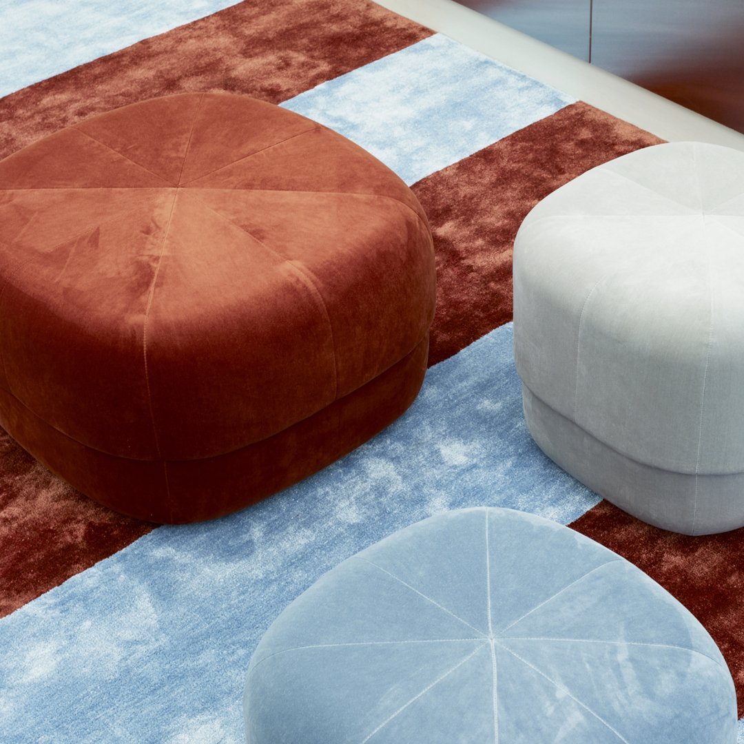 Soft fabric poufs in terracotta, white, and light blue, set against a textured red and blue striped background.
