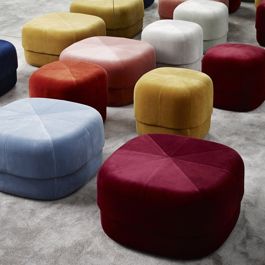 Vibrant assortment of plush poufs in bold reds, soft blues, warm yellows, and muted pinks, featuring quilted patterns.