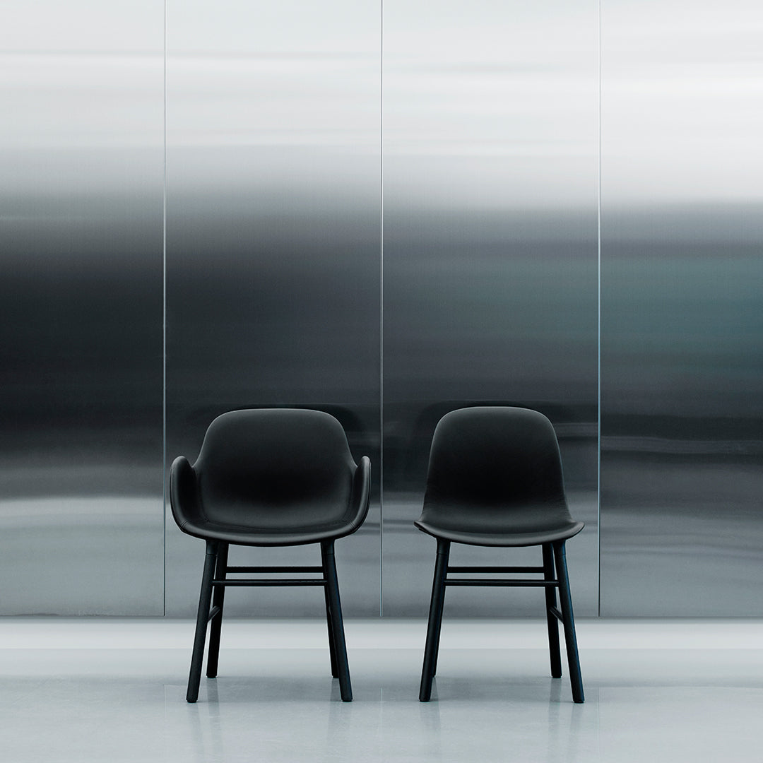 Two sleek black chairs with smooth curves against a reflective silver backdrop, showcasing modern design elements.