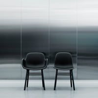Two sleek black chairs with smooth curves against a reflective silver backdrop, showcasing modern design elements.