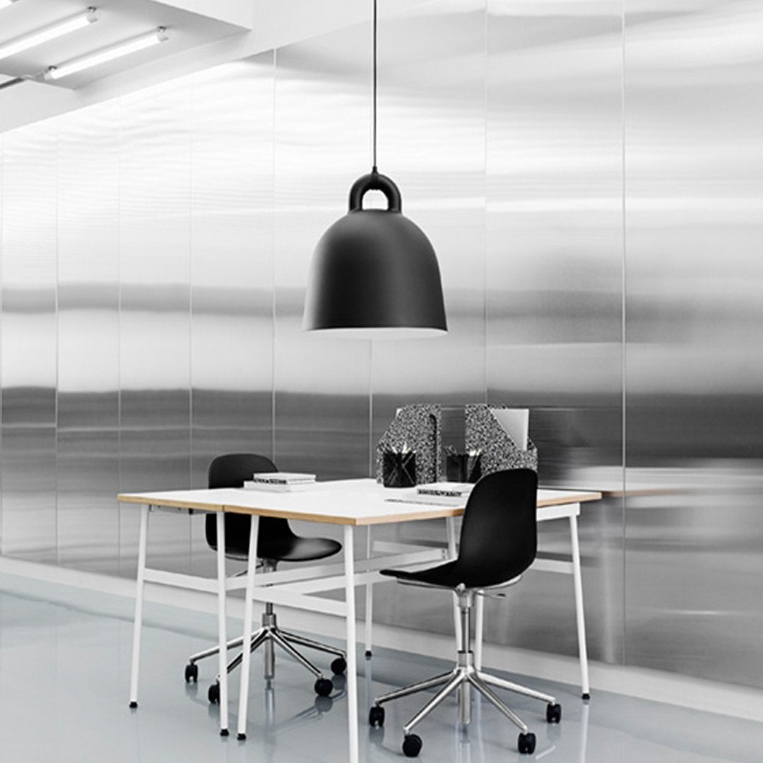 Modern workspace featuring a sleek black lamp, white table, and minimalist black chairs against a metallic silver backdrop.