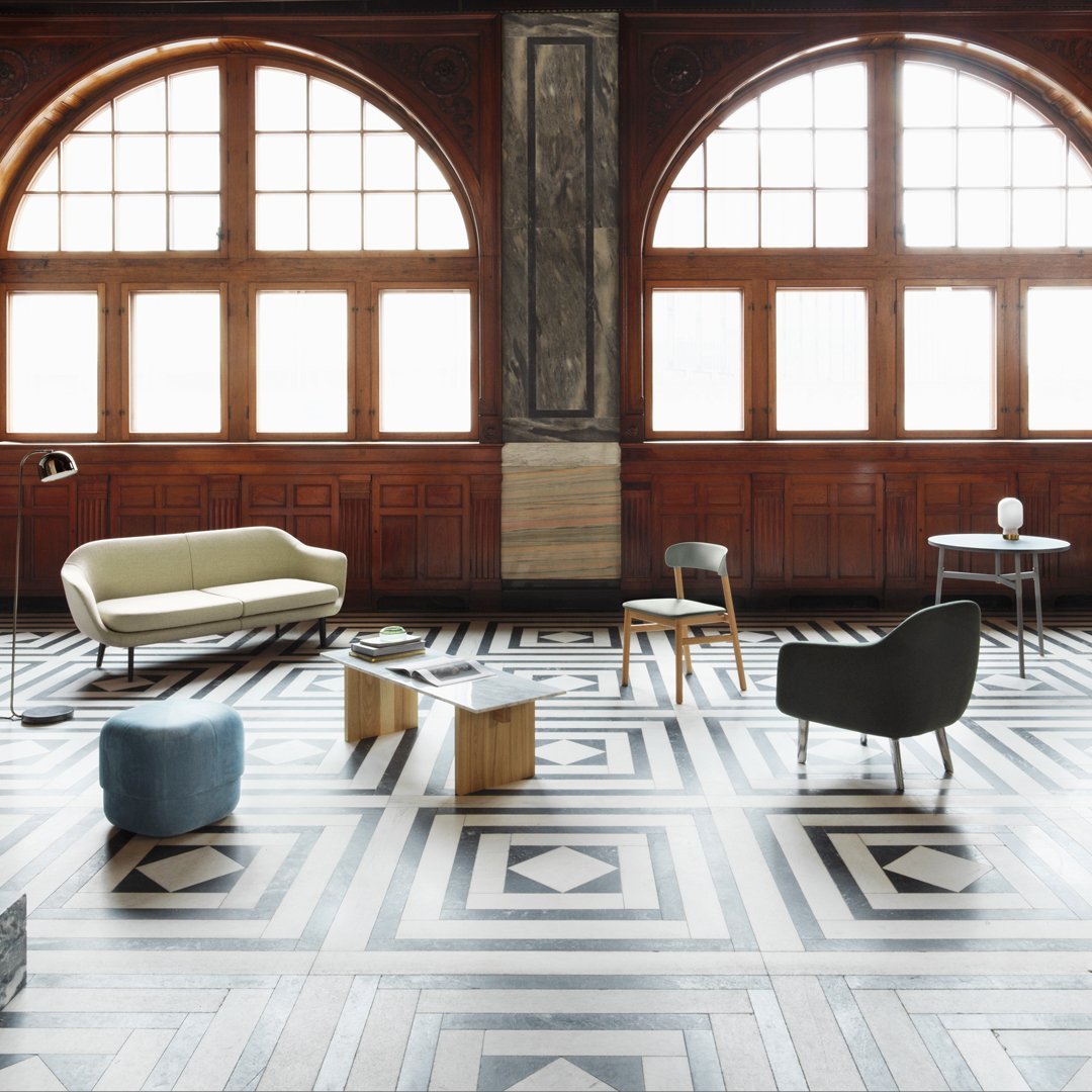 Stylish living room with geometric black and white patterned flooring, green sofa, and gray and blue accent pieces.