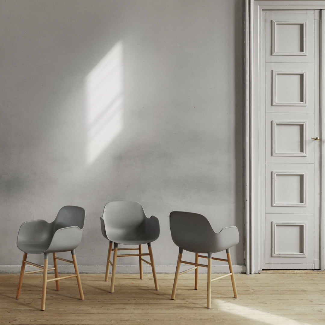 Set of three sleek gray chairs with wooden legs against a minimalist light gray wall. Modern design and soft curves.
