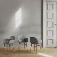 Set of three sleek gray chairs with wooden legs against a minimalist light gray wall. Modern design and soft curves.