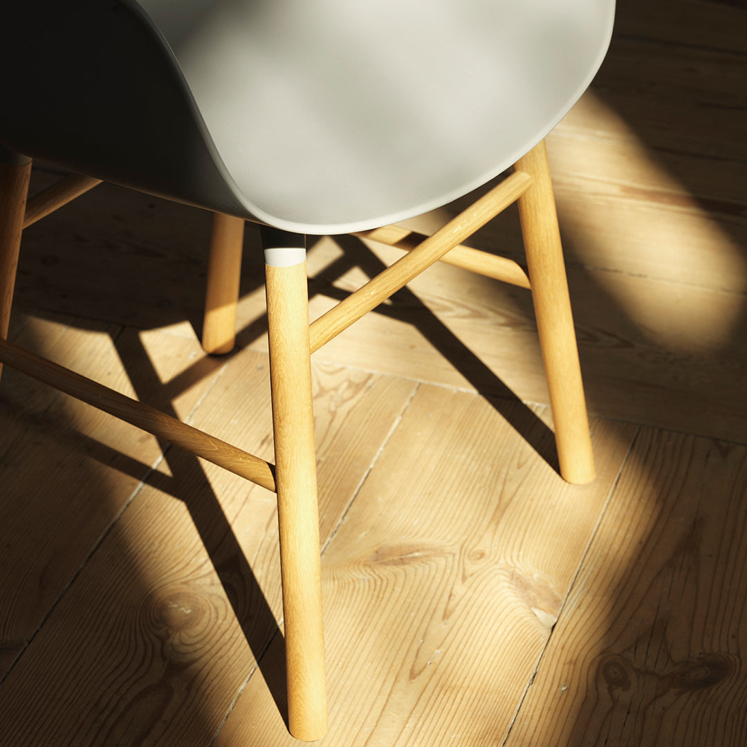 Gray chair with natural wood legs, featuring soft curves and clean lines, set on a warm, light wooden floor.