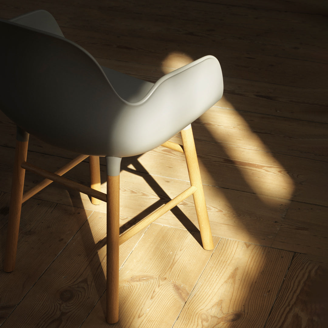 Gray chair with a smooth finish and wooden legs, set against a warm wooden floor, highlighting natural light.