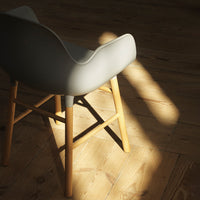 Gray chair with a smooth finish and wooden legs, set against a warm wooden floor, highlighting natural light.