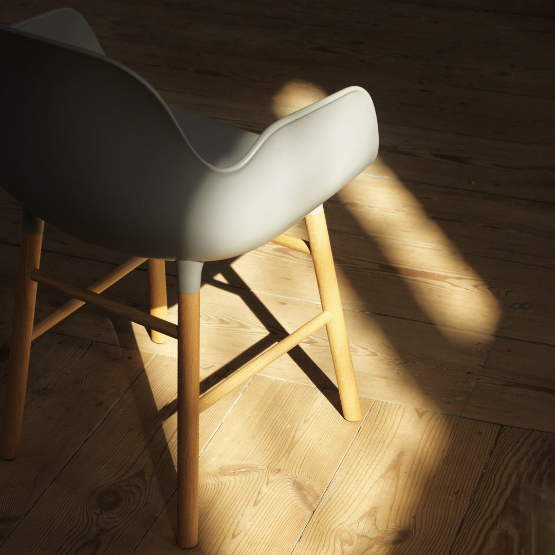 Gray upholstered chair with wooden legs, featuring a smooth, rounded back against a sunlit wooden floor.