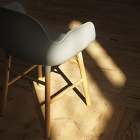Gray upholstered chair with wooden legs, featuring a smooth, rounded back against a sunlit wooden floor.