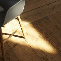 Modern chair with a gray seat and natural wood legs on light wooden floor, highlighted by soft sunlight.