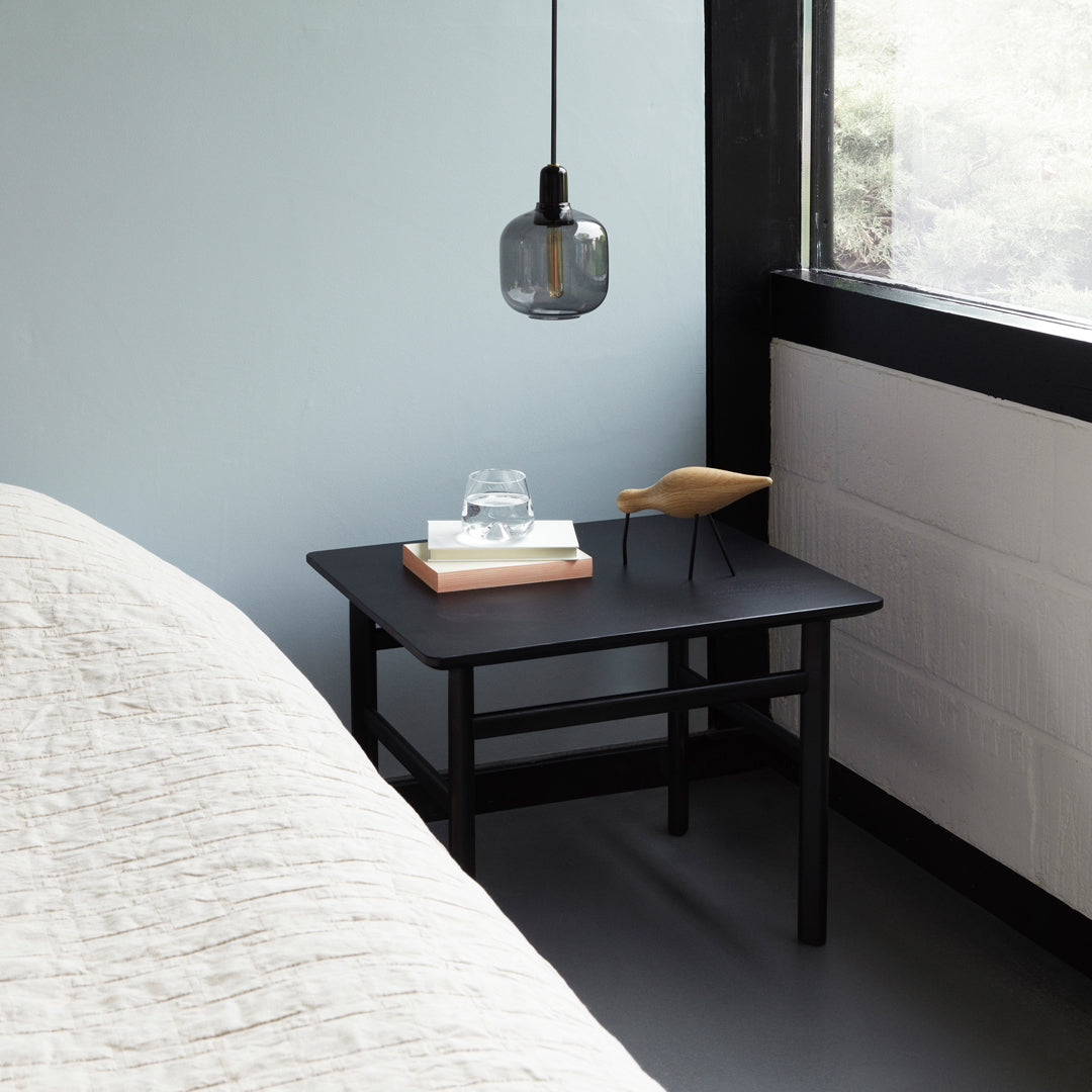 Black wooden side table with a minimalist design, complemented by neutral gray and soft white tones in the room.
