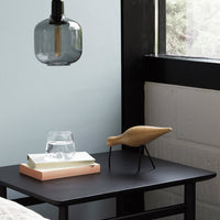 Wooden bird sculpture on black table with a clear glass, minimalist lamp, and pastel background. Modern decor.