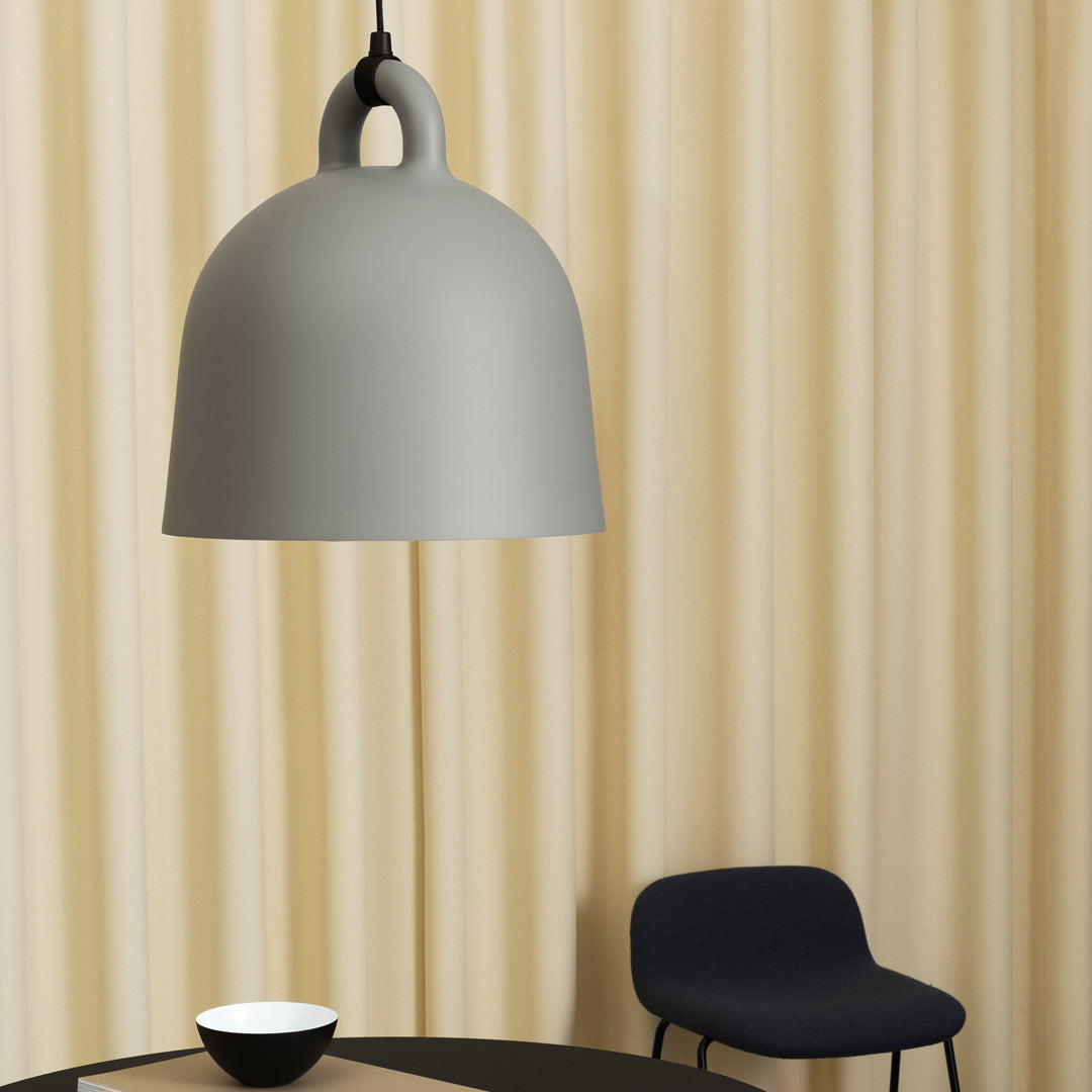 Gray dome pendant light against soft, textured beige curtains and a dark blue chair, creating a modern aesthetic.