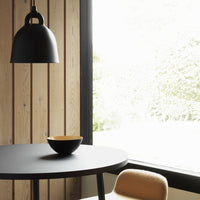 Black pendant light, round black table, and a yellow-accented bowl on a natural wood backdrop with soft natural light.