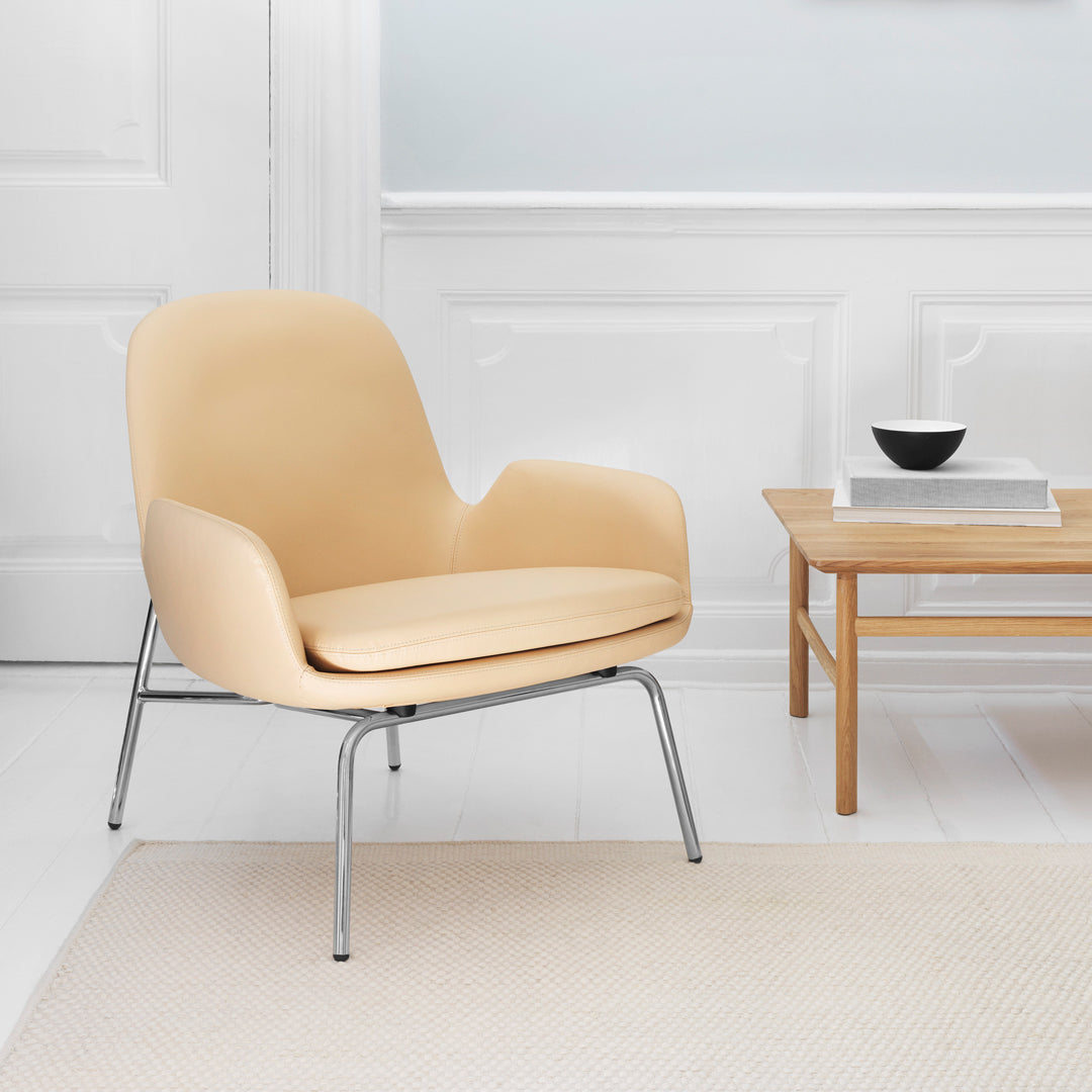 Creamy beige accent chair with smooth curves and sleek chrome legs, set against a minimalist backdrop.