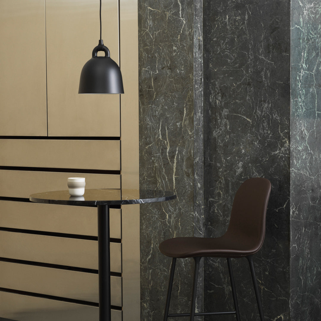 "Black pendant light, marble grey wall, gold-patterned cabinetry, and a brown chair beside a round black table."